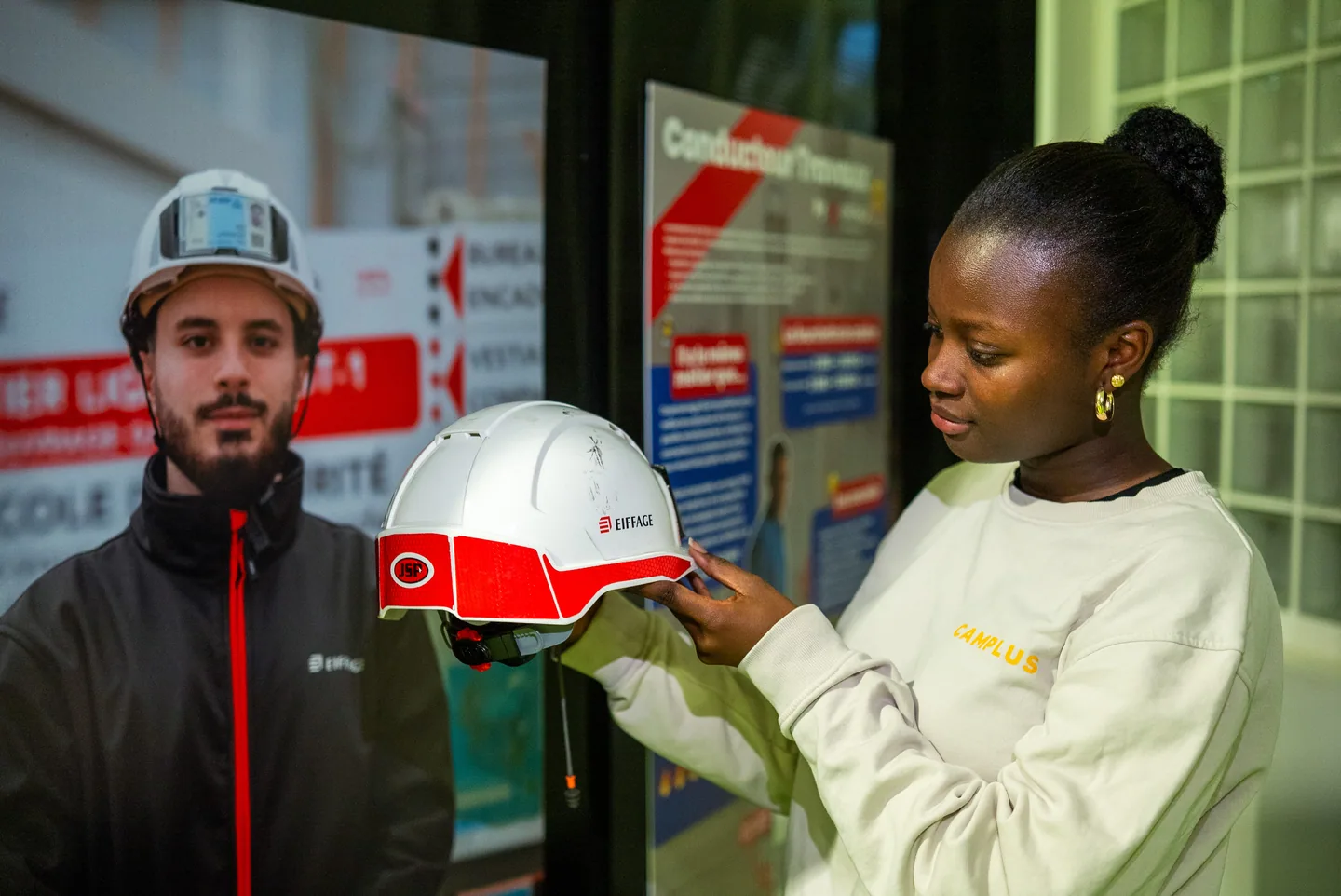 Visiteuse manipulant un casque de chantier dans une exposition Imagine